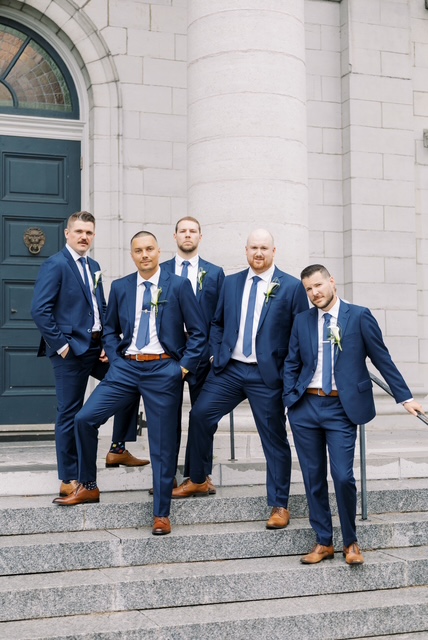 Wedding party in blue suits outside a stone building