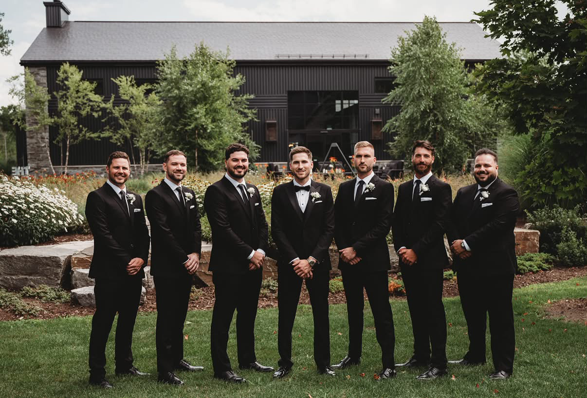 Groom and groomsmen in dark suits outside a wedding venue